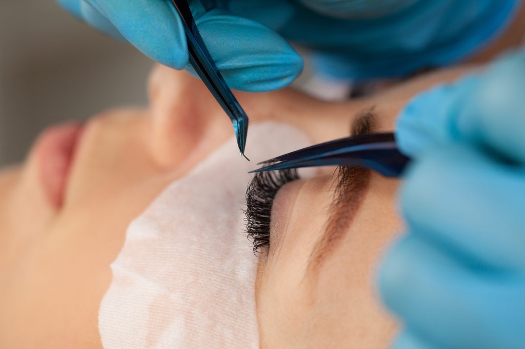 Eyelash extension procedure, a professional stylist lengthens women eyelashes.